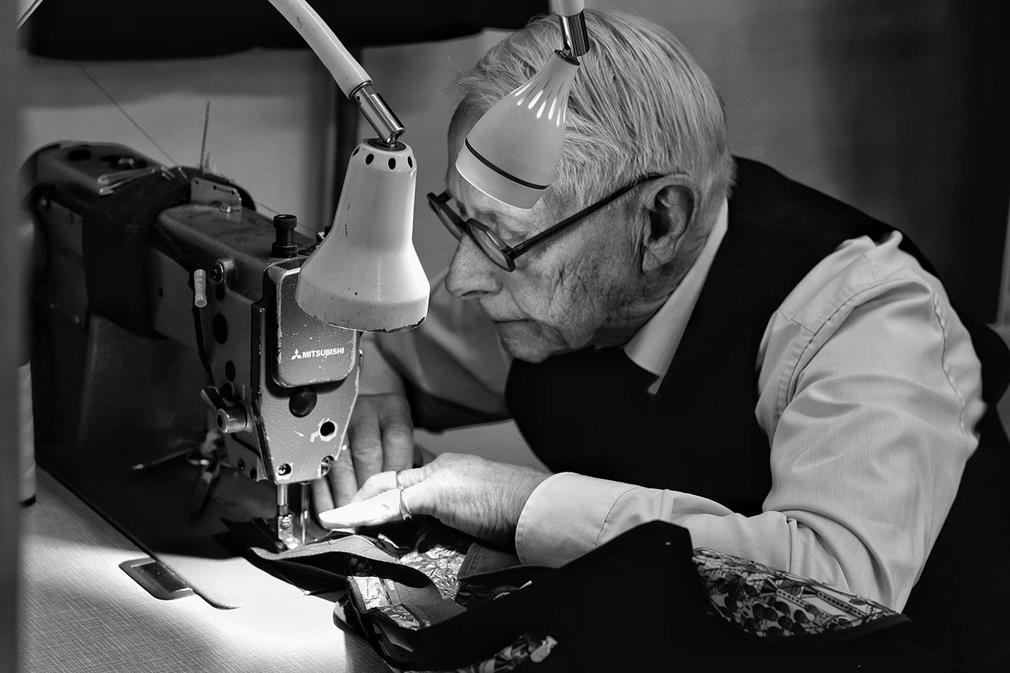 Photographie en noir et blanc d'un couturier expérimenté travaillant à sa machine à coudre en maniant le tissu