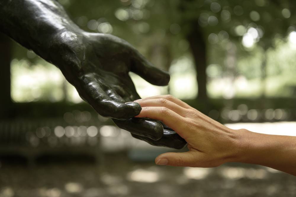main humaine touchant la main d'une statue de Rodin