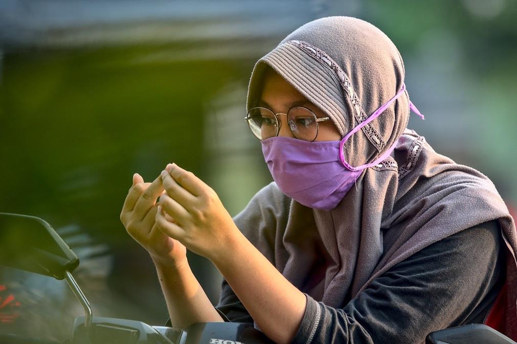 Jeune femme indonésienne portant un masque de protection et observant ses doigts
