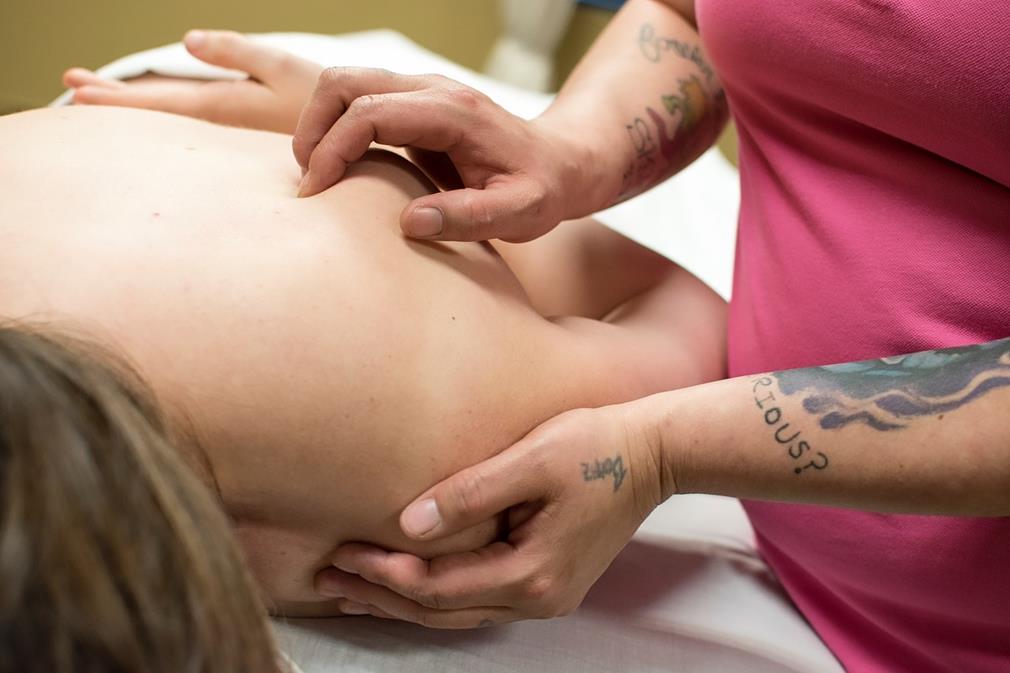 Une séance de massage thérapeutique de type Shiatsu: la patiente est couchée sur le ventre, tandis qu'en gros plan, la main droite de la thérapeute pince lentement des points du dos pendant que sa main gauche apporte un soutien sous l'épaule, par petites pressions et glissements