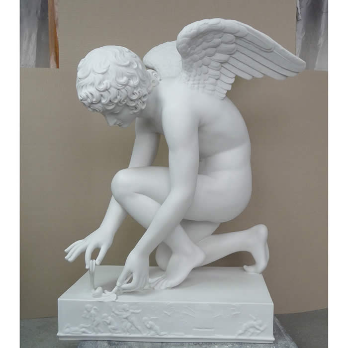 La sculpture l'Amour au papillon: un ange à l'apparence d'un jeune homme est penché, un genou à terre, de profil et manipule délicatement un papillon posé au sol. La statue repose sur un socle.