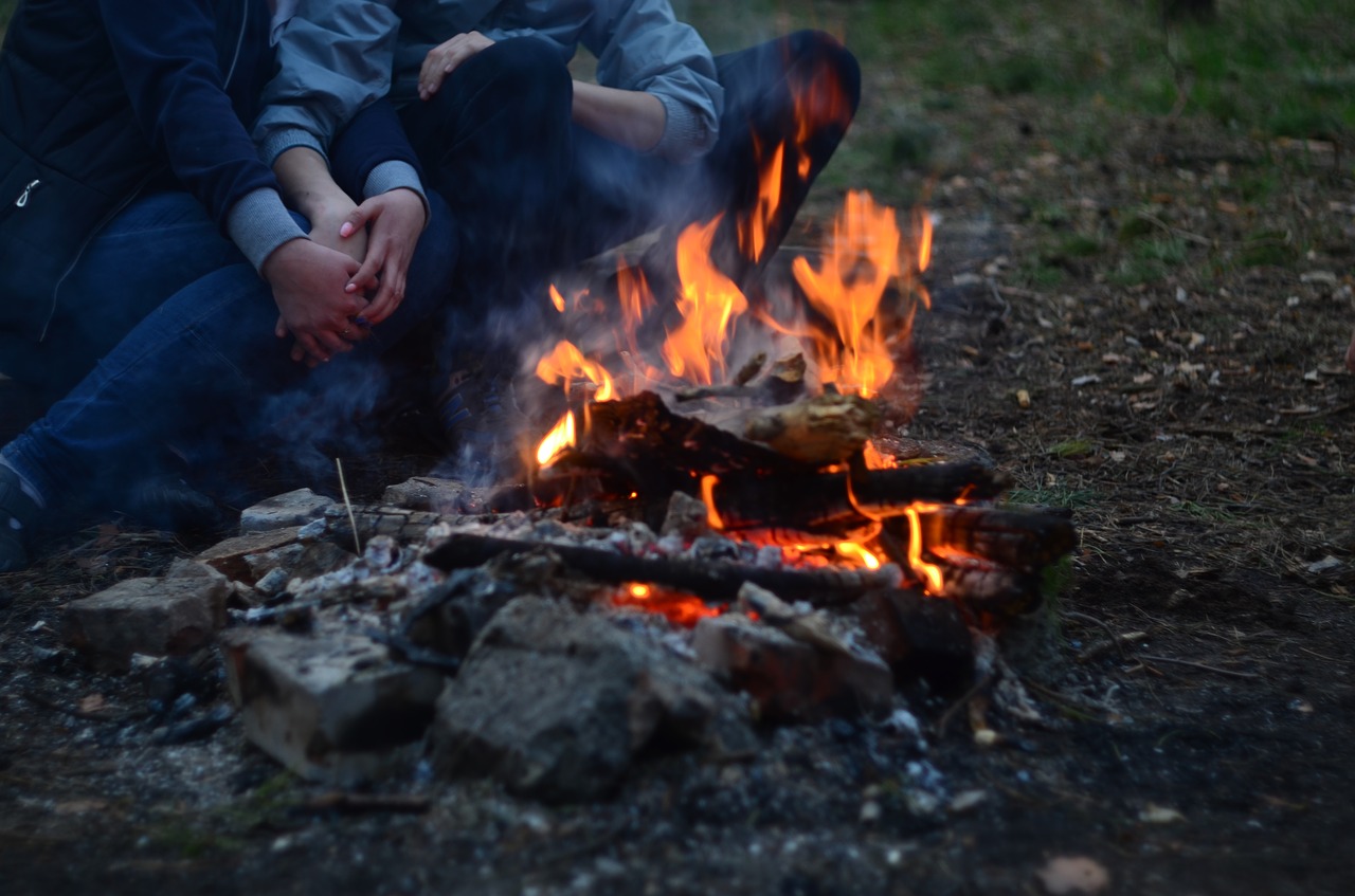 Deux personnes entrelacent leurs jambes et leurs mains autour d'un feu de camp en forêt.