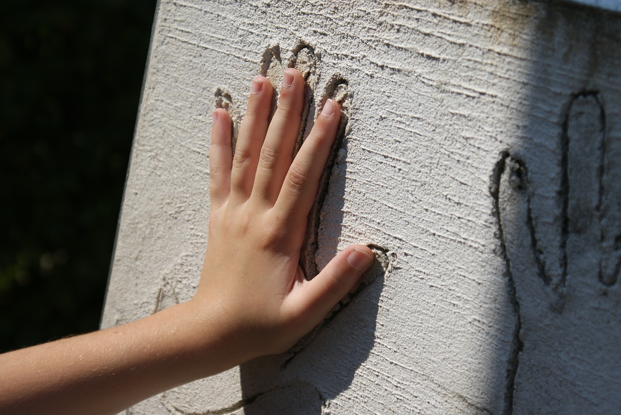 Une main se pose à plat sur un mur de plâtre: sur la surface rugueuse, la main vient se positionner dans une empreinte découpée en relief. D'autres empreintes de mains sont visibles sur le même principe