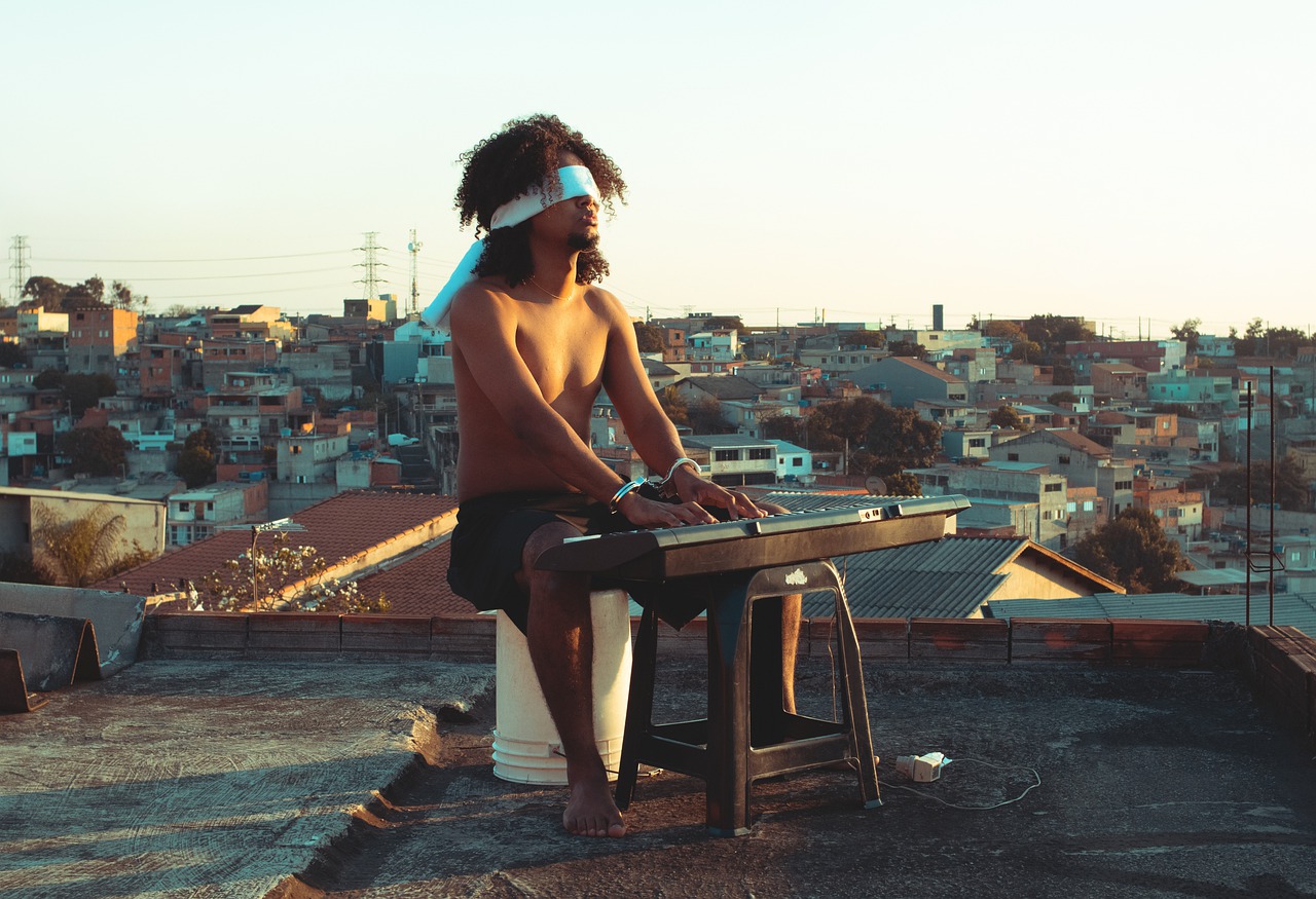 Seul sur un toit-terrasse surplombant les toits anciens d'une ville, un homme s'entraîne à jouer du piano les yeux bandés. Son assise et l'installation du clavier portatif semblent de fortune. Il joue torse nu dans le soleil couchant.
