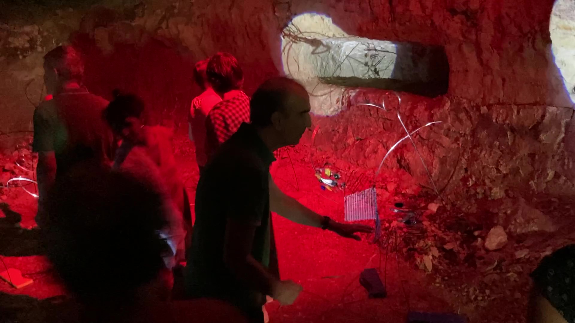 Visite d'une oeuvre d'art en volume exposée dans une grotte troglodyte. Les participants se déplacent dans l'habitat et font bouger, en les touchant, des personnages faits de câbles d'acier.