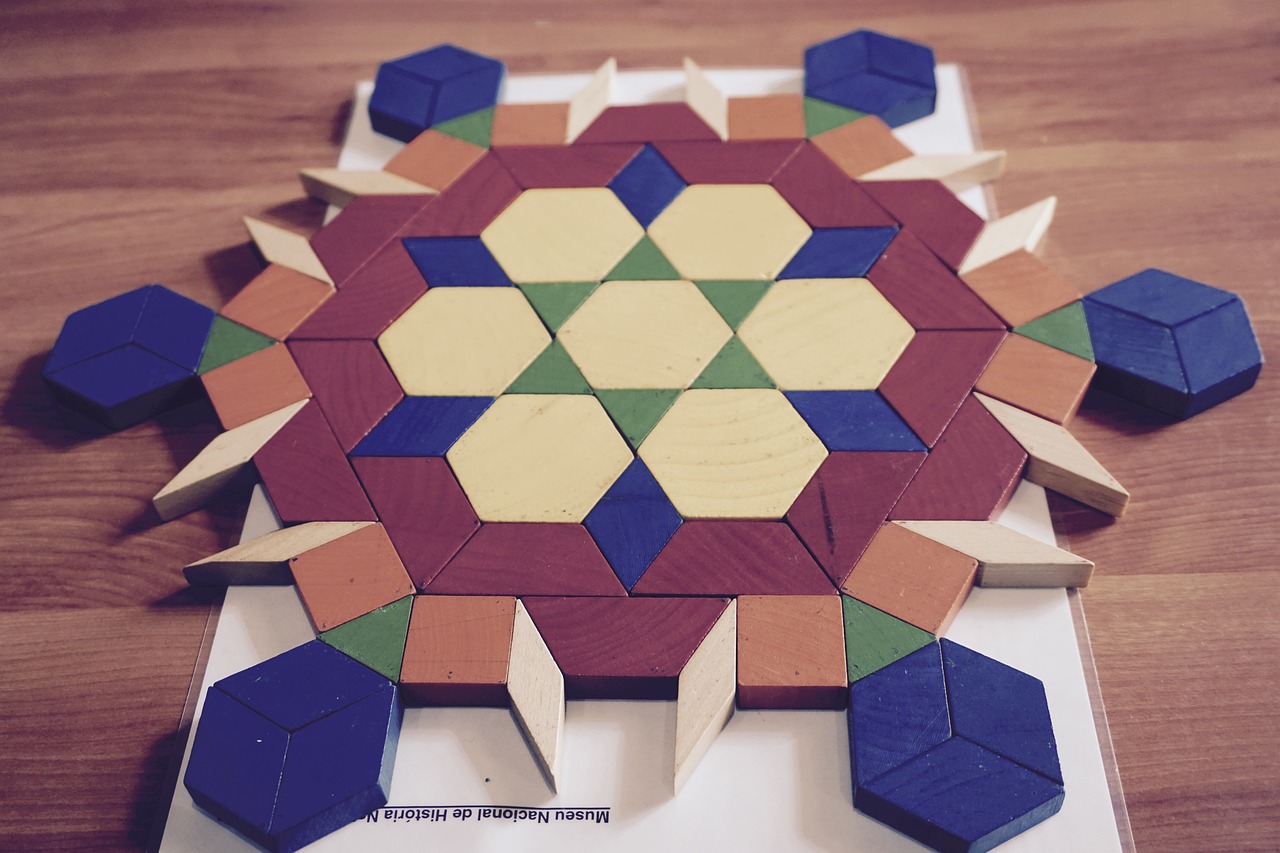 Sur une table, accompagné d'une feuille de consignes, un tangram terminé : des pièces de formes et couleurs variées construisent un mandala aux extrémités tantôt rondes, tantôt pointues