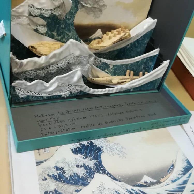 La célèbre vague d'Hokusaï. Dans une boîte à archives, les différents plans sont présentés les uns derrière les autres pour montrer la profondeur entre les barques, les mouvements de la vague, la montagne. Les éléments comme l'écume sont divers morceaux de tissu, dentelle notamment.