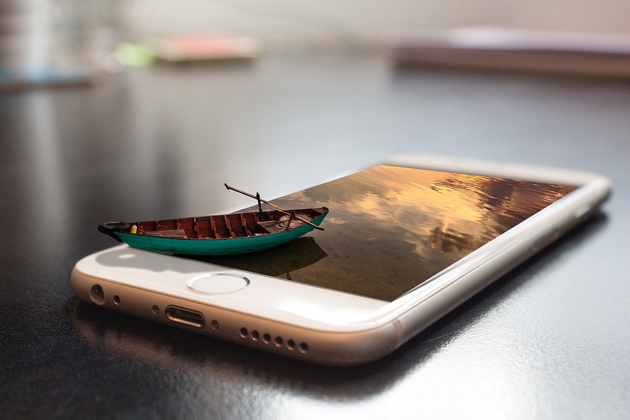Un smartphone posé à plat sur une table. Sur l'écran, la surface d'un lac. Une barque avec rames mais sans passager est sortie de l'écran et apparaît en relief pour voguer sur la surface d'eau virtuelle.