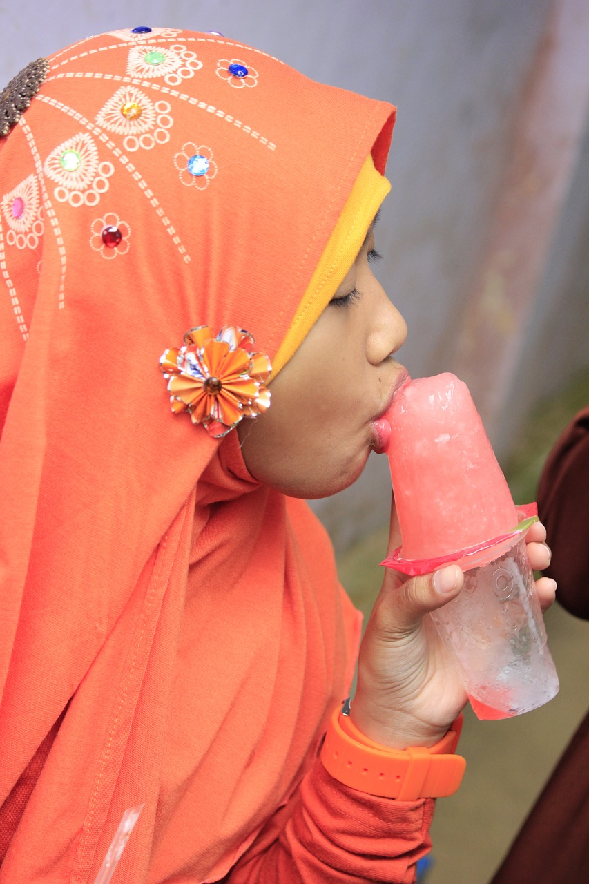 De profil, une femme en tenue indonésienne (sari et tête voilée, tissu coloré et décoré de fleurs) applique ses lèvres sur une glace, dans un mouvement de succion. L'emballage du yaourt glacé fait office de cornet.