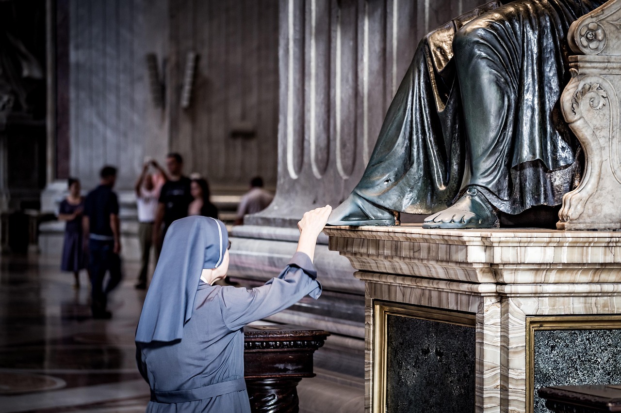 Dans la Basilique de Rome, une religieuse en tenue de Sœur, de profil, est en train de toucher le pied droit de la statue de Saint-Pierre assise sur son trône et qu'on ne distingue que jusqu'aux genoux.
