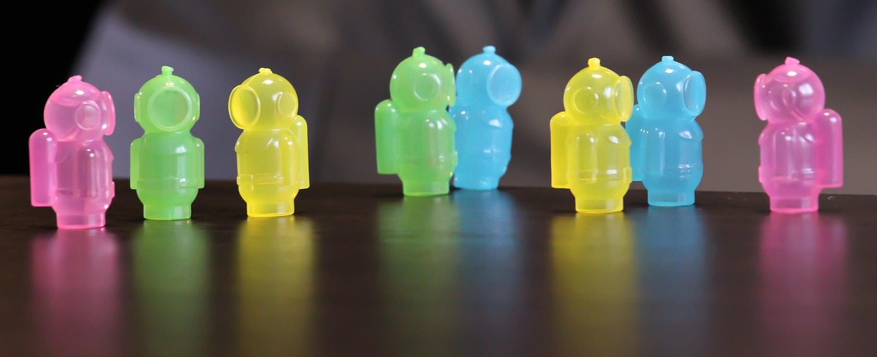 Posés sur une table, huit petits jouets représentant des bonshommes en scaphandre, chacun d'une couleur différente (rose, vert, jaune et bleu) et lumineux, alignés comme une guirlande. Tournés les uns vers les autres, en trio ou en duo comme s'ils s'adressaient les uns aux autres.