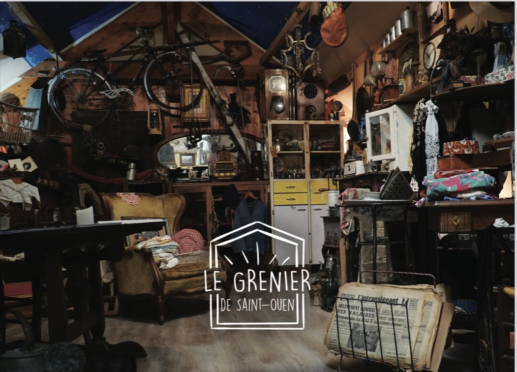 Photo du grenier en question. Comme tous les greniers, sous les combles, des meubles (bureau, fauteuils, armoires, etc) tous recouverts d'objets en tous genres. Au mur, des vélos accrochés, des journaux empilés dans des porte-revues ; toutes les surfaces sont recouvertes et des éléments pendent des poutres et des murs.